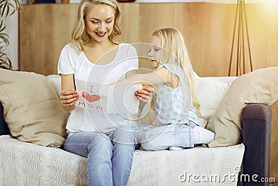 Happy mother day in sunny flat. Child daughter congratulates mom and gives her postcard with heart drawing. Family Stock Photo