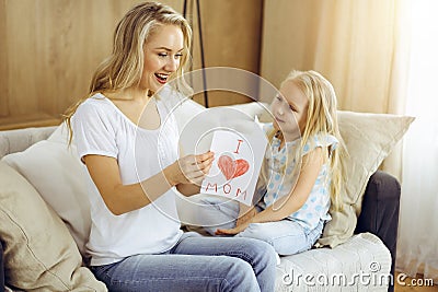 Happy mother day in sunny flat. Child daughter congratulates mom and gives her postcard with heart drawing. Family Stock Photo