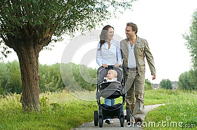 Happy mother and father walking with baby in pram Stock Photo