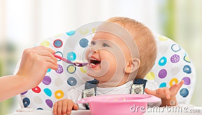 Happy mother feeds funny baby from spoon Stock Photo