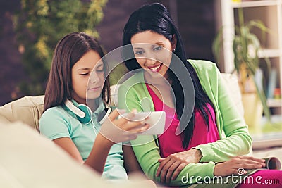 Happy mother and her cute teen daughter are looking at mobile phone Stock Photo