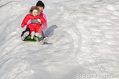 Happy mother and her daughter enjoying a sledge ride down the hils Stock Photo