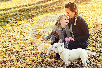 Happy mother and her daughter playing with dog in autumn park. Family, pet, domestic animal and lifestyle concept. Autumn time. Ha Stock Photo