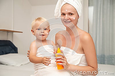 Happy mother and infant baby in white towels after bathing apply sunscreen or after sun lotion or cream. Children skin care. Spf, Stock Photo