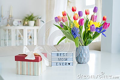 Happy Mother`s Day background. Colorful spring flowers bouquet in vase, gift box with satin ribbon and lightbox with words Best Stock Photo