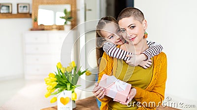 Happy Mother`s Day or Birthday Background. Adorable young girl surprising her mom, young cancer patient, with bouquet and present. Stock Photo