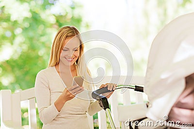 Happy mother with smartphone and stroller in park Stock Photo