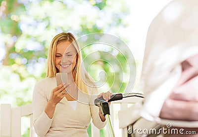 Happy mother with smartphone and stroller in park Stock Photo