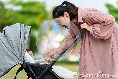 happy mother talking and playing with her infant baby in the stroller while resting in park Stock Photo