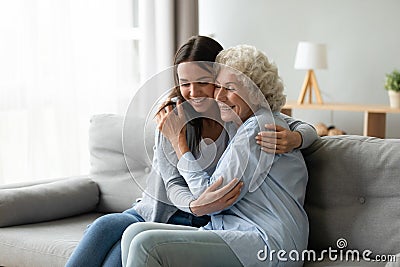 Elderly grandmother snuggle to grownup granddaughter seated on couch Stock Photo