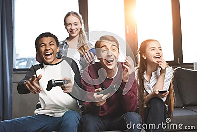 Happy multicultural teenagers playing video games with joysticks at home Stock Photo