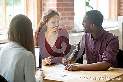 Happy multiethnic couple looking at each other before signing co Stock Photo