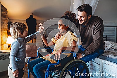 Happy multiethnic family. Smiling little girl with disability in wheelchair at home Stock Photo