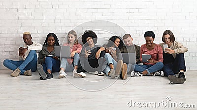 Happy multiethnic millennials using gadgets while spending time together Stock Photo