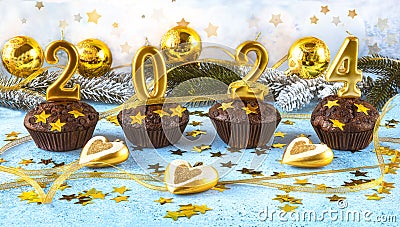 Happy new year 2024 concept. Bright candles, chocolate muffins, Christmas tree toys, balls and golden confetti Stock Photo