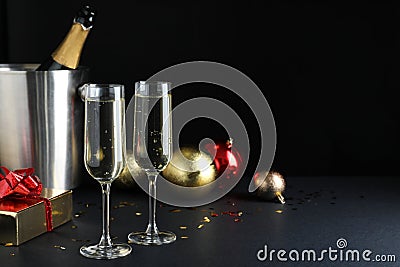 Happy New Year! Glasses with sparkling wine, bottle in bucket and festive decor on table against black background, space for text Stock Photo