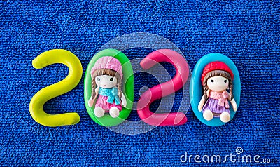 Happy New Year 2020 , molding of color clay with little girls toys on blue background. Stock Photo