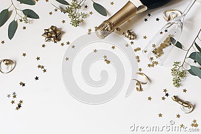 Happy New Year still life. Empty champagne glass, wine bottle with golden confetti stars and eucalyptus branches Stock Photo