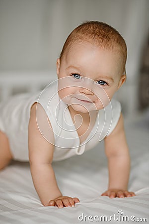 A happy newborn baby crawls on the bed and smiles. Stock Photo