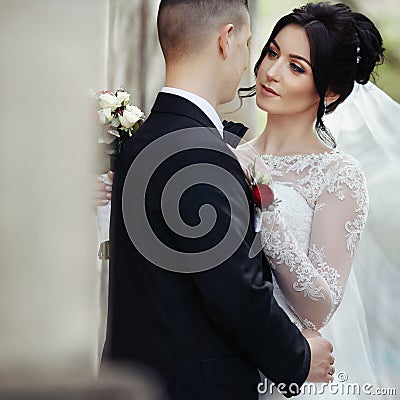 Happy newlywed brunette bride hugging handsome groom near old wa Stock Photo