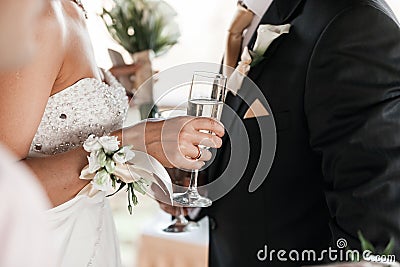 Happy newlyweds couple drink white wedding champagne wine.Decorated crystal glasses.Hands of bride and groom with gold Stock Photo