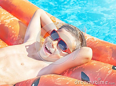 Happy nine years old child boy in red sunglasses playing with inflatable ring air mattress in swimming pool. Caucasian kid. Stock Photo