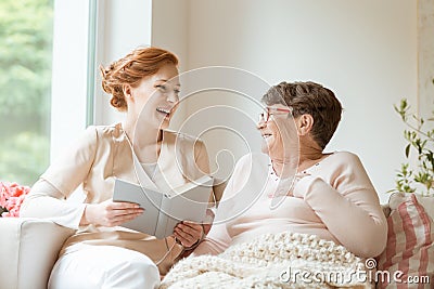 Happy nurse reading a funny book to her elderly patient in a private nursing home Stock Photo