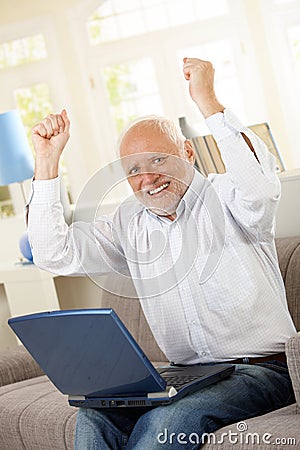 Happy old man sitting on sofa with laptop Stock Photo