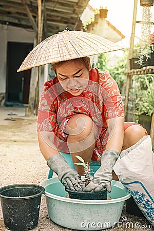 Happy old Thai gardener woman in vietnamese straw hat potting flowers in her garden Stock Photo