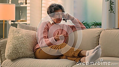 Happy old woman relaxing on cozy sofa talking on smartphone smiling senior grandma at comfy couch at home distant talk Stock Photo