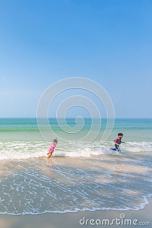 Happy older brother and little sister playing and surfing on white sand beach, light blue sky backgrounds. Summer season. Sunny Editorial Stock Photo