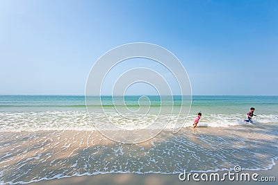 Happy older brother and little sister playing and surfing on white sand beach, light blue sky backgrounds. Summer season. Sunny Editorial Stock Photo