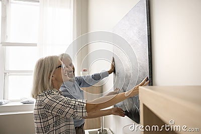 Happy older couple hanging picture on wall at home Stock Photo