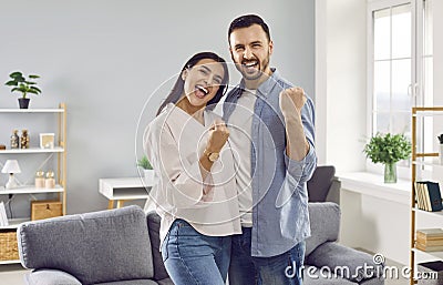 Happy overjoyed couple family with yes gesture standing in the living room at home. Stock Photo