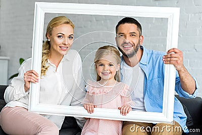 happy parents with adorable little daughter holding white frame and smiling Stock Photo