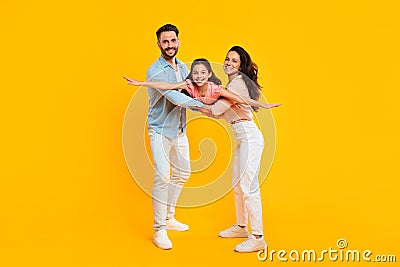 Happy parents holding daughter, girl spreading arms like plane, posing, having fun over yellow background, full length Stock Photo