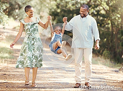 Happy parents swing girl at their hands in the forest during a walk in nature. Cheerful kid having fun while bonding Stock Photo