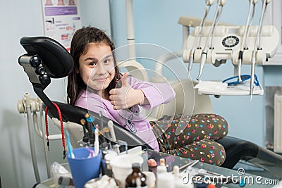 Happy patient girl showing thumbs up at dental clinic office. Medicine, stomatology and health care concept Stock Photo