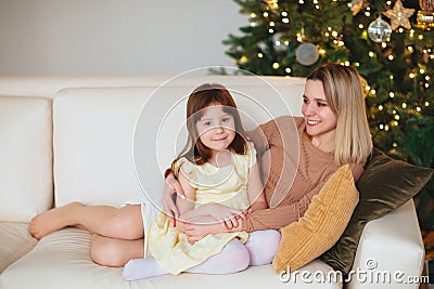 Happy playful little girl daughter playing with positive mother, jumping on sofa, spending time together during Christmas holidays Stock Photo