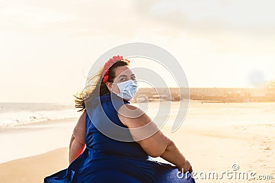 Happy plus size woman walking on the beach while wearing face mask - Curvy overweight model having fun during vacation Stock Photo