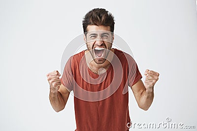 Happy positive excited young man clenching fists and screaming, wearing casual t-shirt glad to hear good news Stock Photo