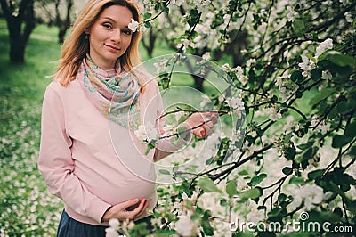 Happy pregnant blonde beautiful woman walking outdoor in spring park or garden Stock Photo