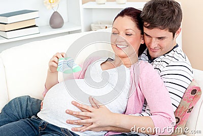 Happy pregnant woman holding baby shoes at home