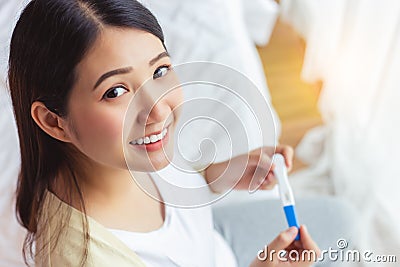 Happy pregnant woman holding pregnancy test and get happy because single mother has baby with smiley face. Young Mother waiting Stock Photo