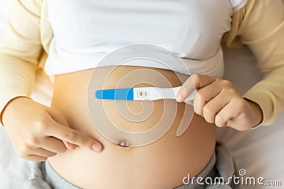 Happy pregnant woman holding pregnancy test pointing finger to beautiful belly that pregnant girl has fetus inside. Young Mother Stock Photo