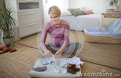Happy pregnant woman looking at little clothes for her baby. Stock Photo