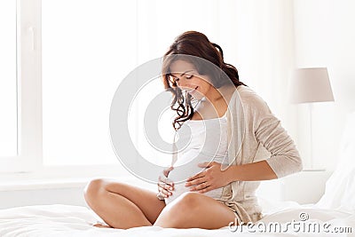 Happy pregnant woman sitting on bed at home Stock Photo