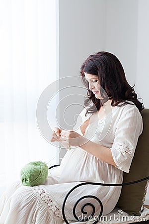 Happy pregnant woman in white dress knitting Stock Photo