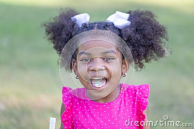 Happy preschooler African girl sticking his tongue out with candy, Kid girl playing outdoors in the park Stock Photo