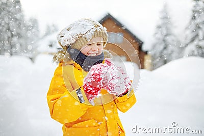 Happy preteen boy having fun playing with fresh snow during snowfall in european Alps. Child dressed in warm clothes, hat, hand Stock Photo